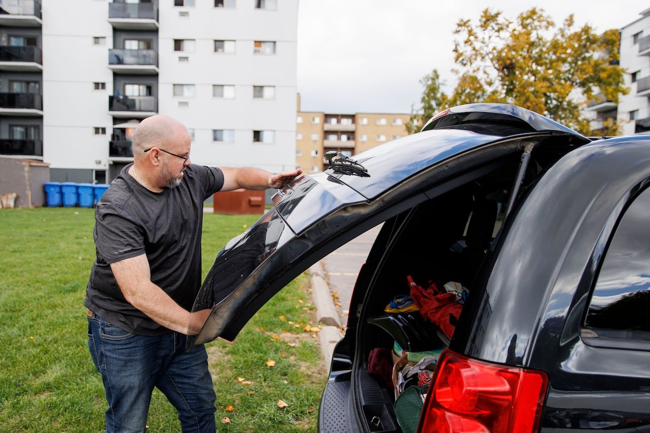 Photo of a man in a grey shirt closing a car boot.