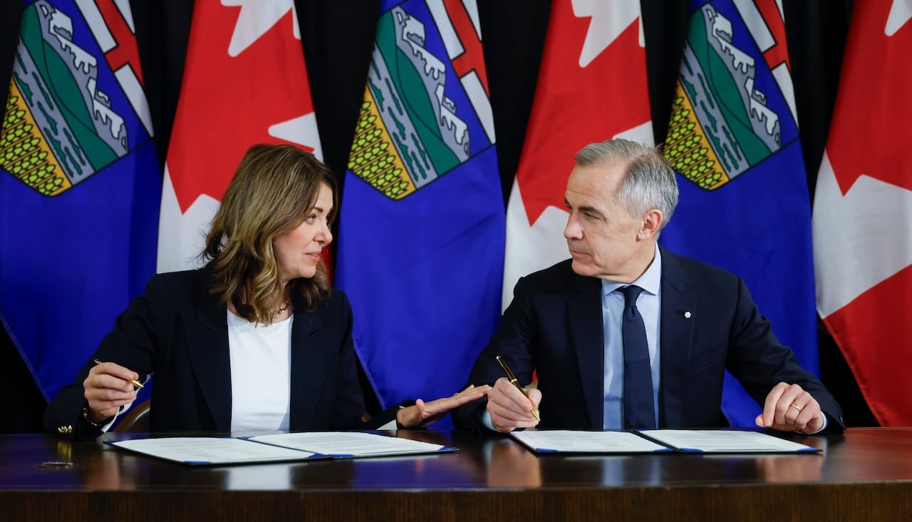 A woman and a man in business attire discussing at a table with Canadian and Alberta flags in the background.
