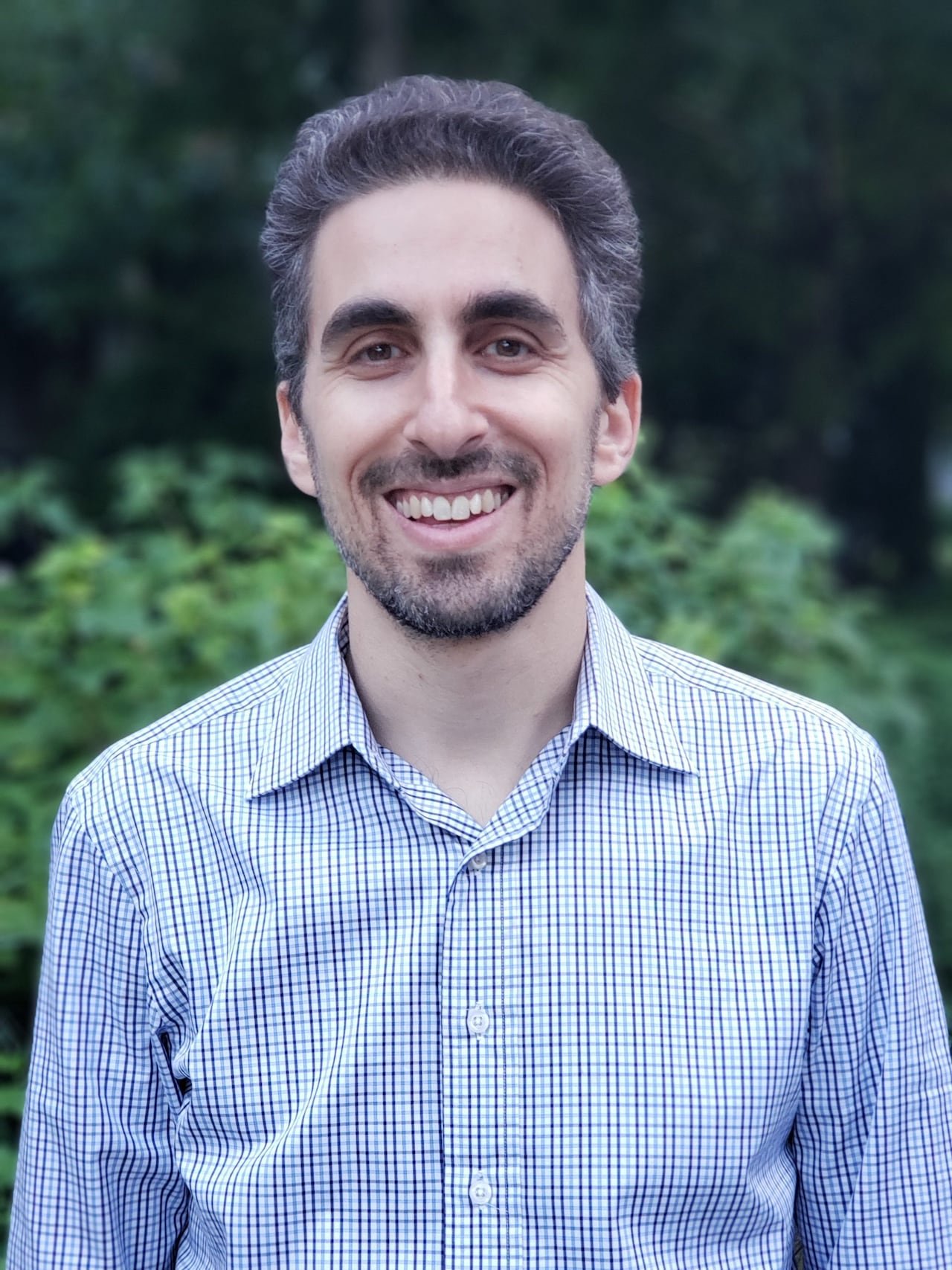 A man in a checkered shirt with a beard smiling at the camera.