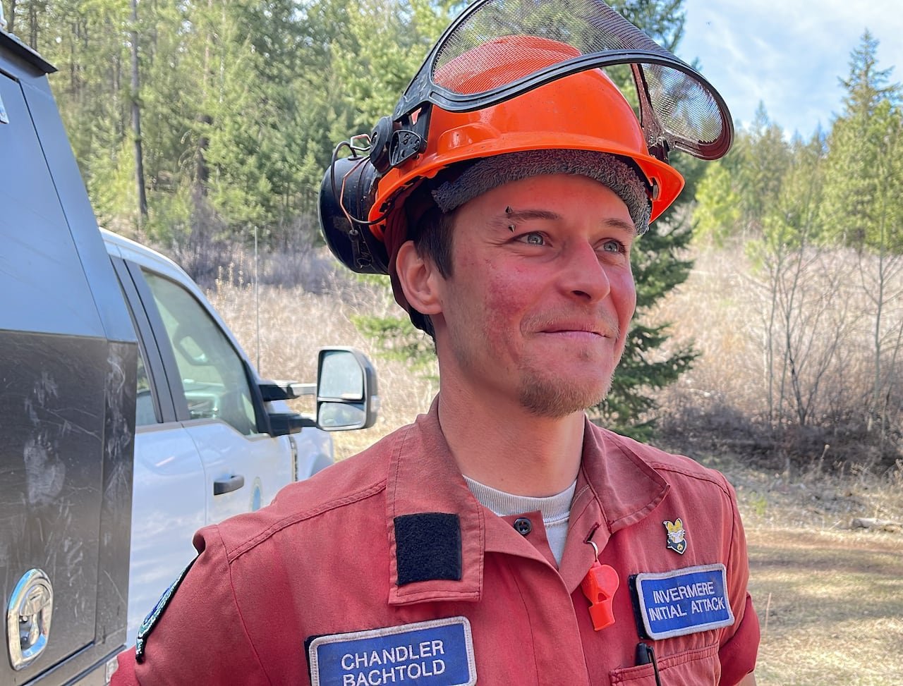 default-411 A firefighter wearing red garments and an orange helmet smiles outdoors.