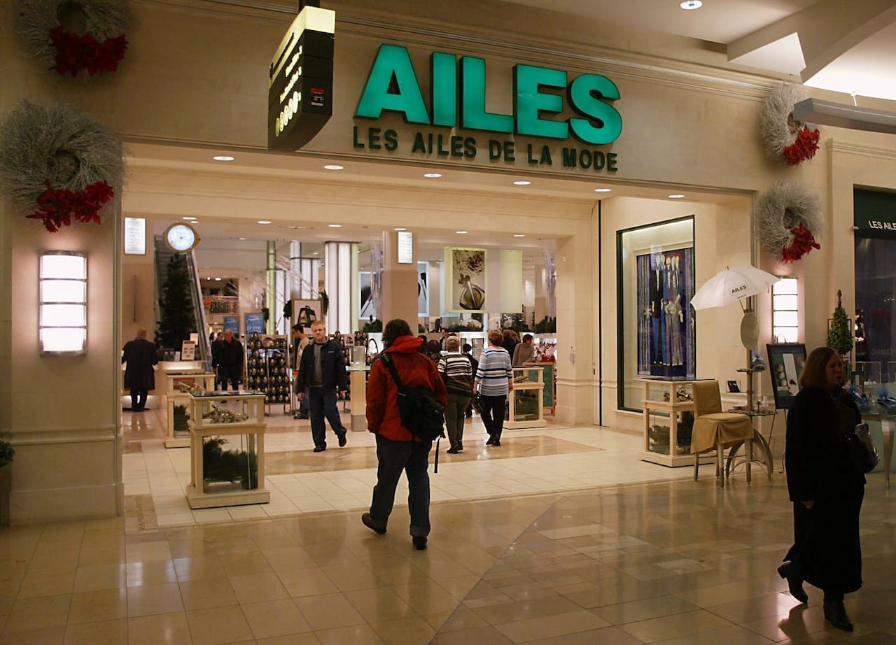 default-1107 People walking by a Les Ailes de la Mode location inside a shopping mall. The shop has a bright green sign