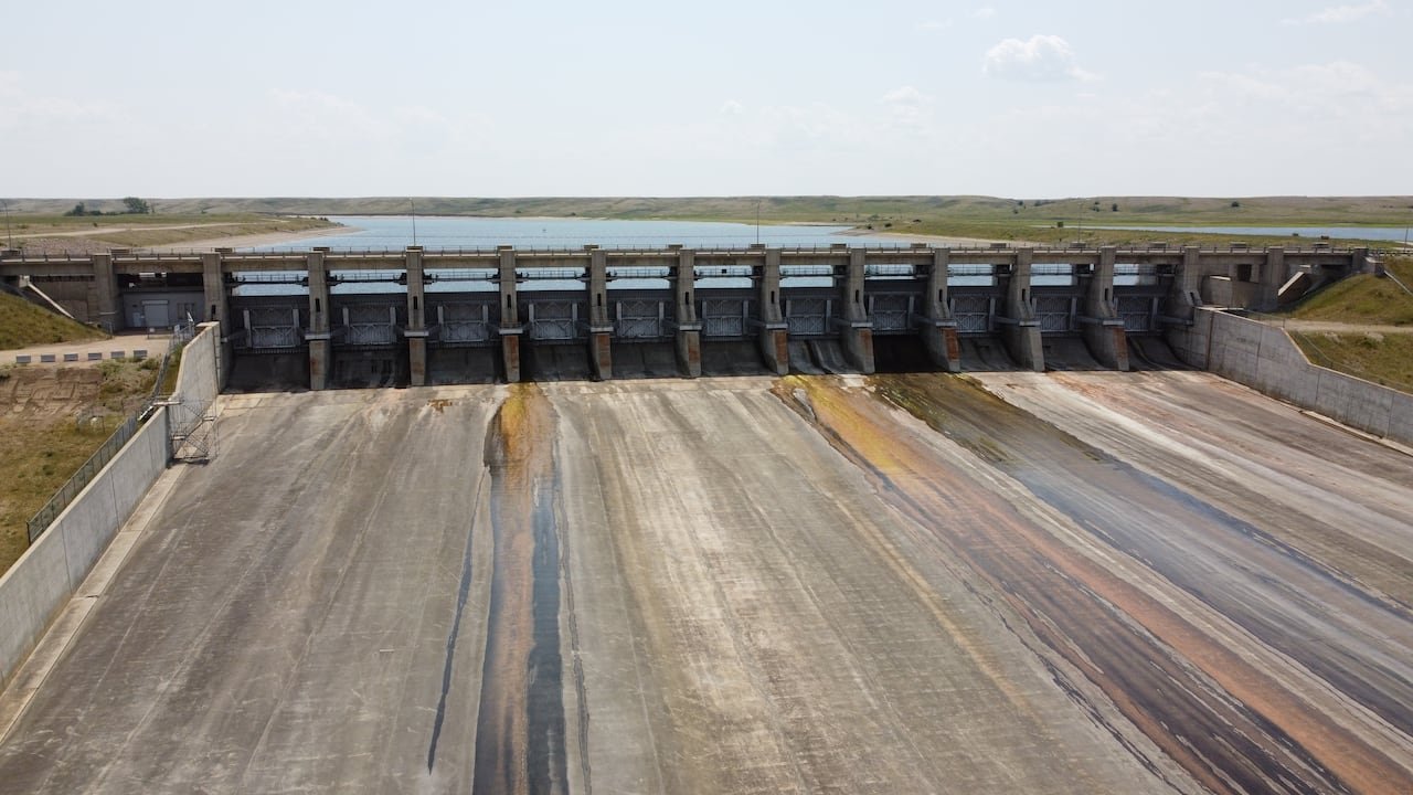 A large concrete structure sits in front of a large lake with vegetation on the side.